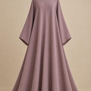 Peut inclure: Une robe longue couleur mauve avec une encolure ronde fendue verticalement et fermée par un bouton unique. Le vêtement présente des manches larges et évasées ainsi qu'une jupe ample et fluide tombant des épaules jusqu'au sol.
