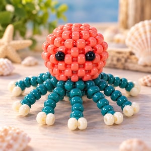 Könnte beinhalten: Eine handgefertigte Oktopus-Figur aus kleinen Kunststoffperlen. Der runde Kopf besteht aus korallenfarbenen Perlen mit zwei glänzenden schwarzen Perlen als Augen. Acht strahlenförmige Tentakel bestehen aus blaugrünen Perlen mit weißen Spitzen.