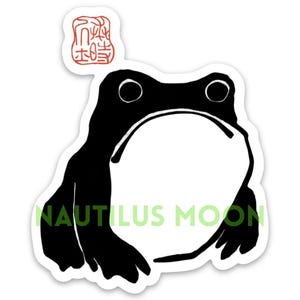 May include: Black and white illustration of a frog with a red stamp above it that says "木蛙".