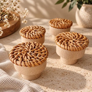 May include: A set of four cabinet knobs, each featuring a circular light wood base and a top surface crafted from woven natural rattan in a light brown color. The knobs have a stepped, cylindrical profile with a flat, textured woven top.