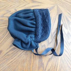 May include: A black fleece bonnet with a lace trim and black ribbon ties.