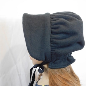 May include: A dark navy blue bonnet with a ruffled crown and a wide brim. The bonnet is made of a soft, fleece-like material and features a black and white striped ribbon tie.