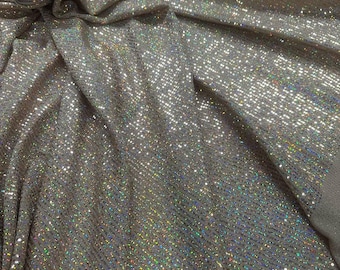 Peut inclure: Un tissu beige scintillant doté d'une surface dense et réfléchissante avec une texture fine et pailletée. Le matériau présente un motif diagonal répétitif subtil qui capte la lumière, créant un éclat irisé multicolore sur les plis.