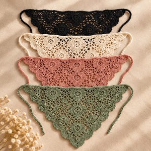May include: Four triangular crochet bandanas arranged vertically in a stack. The colours from top to bottom are black, cream, dusty rose, and sage green. Each piece features a repeating floral lace pattern with scalloped edges and thin tie strings.