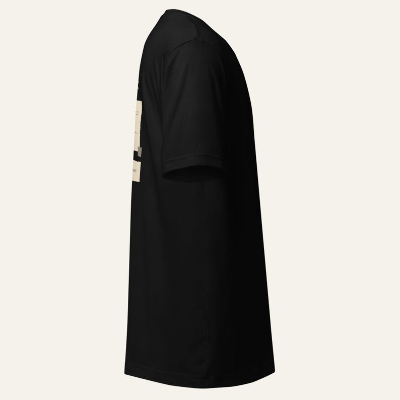May include: A black short-sleeved t-shirt viewed from the side. The garment features a rectangular cream-coloured graphic print on the side panel containing black text. The fabric appears smooth and solid black throughout the rest of the shirt.