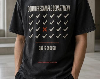 May include: A charcoal gray short-sleeve t-shirt featuring the text COUNTEREXAMPLE DEPARTMENT in white, a grid of white checkmarks with one red X, the text ONE IS ENOUGH, and the website PROOFANDPARTICLE.COM printed in red at the bottom.