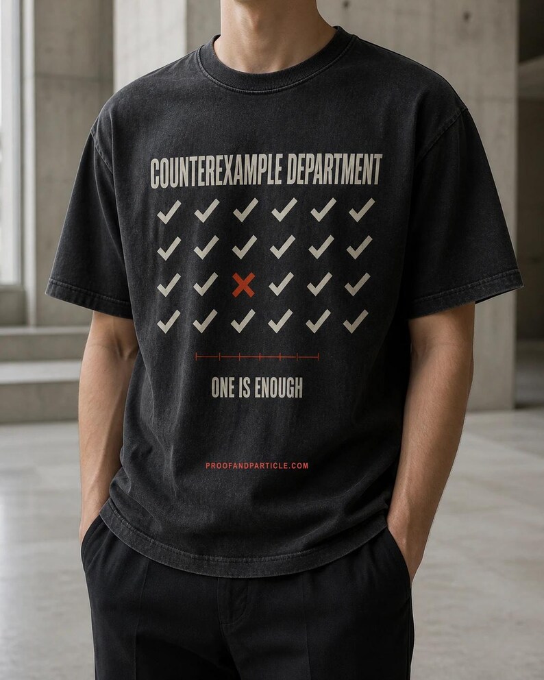 Peut inclure: Un t-shirt gris anthracite &agrave; manches courtes avec le texte COUNTEREXAMPLE DEPARTMENT en blanc, une grille de coches blanches avec une croix rouge, le texte ONE IS ENOUGH et le site PROOFANDPARTICLE.COM imprim&eacute; en rouge en bas.