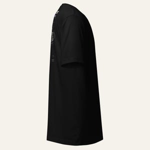 May include: A black short-sleeved t-shirt viewed from the side. The garment features a white graphic print on the upper back area, displaying technical line drawings and text that reads "THE REACTOR" and "CORE" in a clean, sans-serif font style.