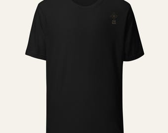 Puede incluir: Una camiseta negra de manga corta con un pequeño gráfico de una flor de cuatro pétalos de líneas finas en la parte superior izquierda del pecho. Debajo de la flor, el texto "HOSE 5:11" está impreso en una fuente sencilla y clara. Cuello redondo.
