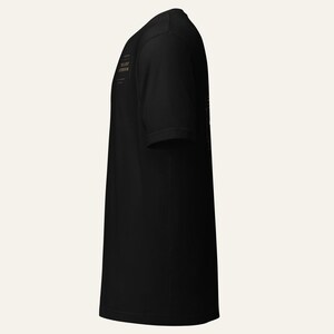 May include: A black short-sleeved t-shirt viewed from the side. The shirt features a small rectangular graphic on the chest area containing the text THE LOST NOTEBOOK in a serif font, enclosed within a thin border with decorative corner accents.
