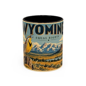 Peut inclure: Un mug cylindrique en céramique avec un intérieur et un bord noirs. L'extérieur présente un graphique représentant une sturnelle jaune perchée sur un poteau en bois, un paysage de montagnes enneigées et le texte WYOMING EQUAL RIGHTS en bleu.