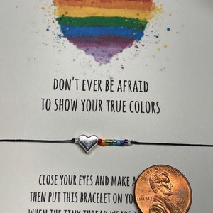 May include: A rainbow heart with the text "Don't ever be afraid to show your true colors."  A black string bracelet with a silver heart charm and rainbow beads. The text "Close your eyes and make a wish, then put this bracelet on your wrist. When the tiny thread wears thin, that is when your wish comes true." is below the bracelet. A penny is in the bottom right corner.