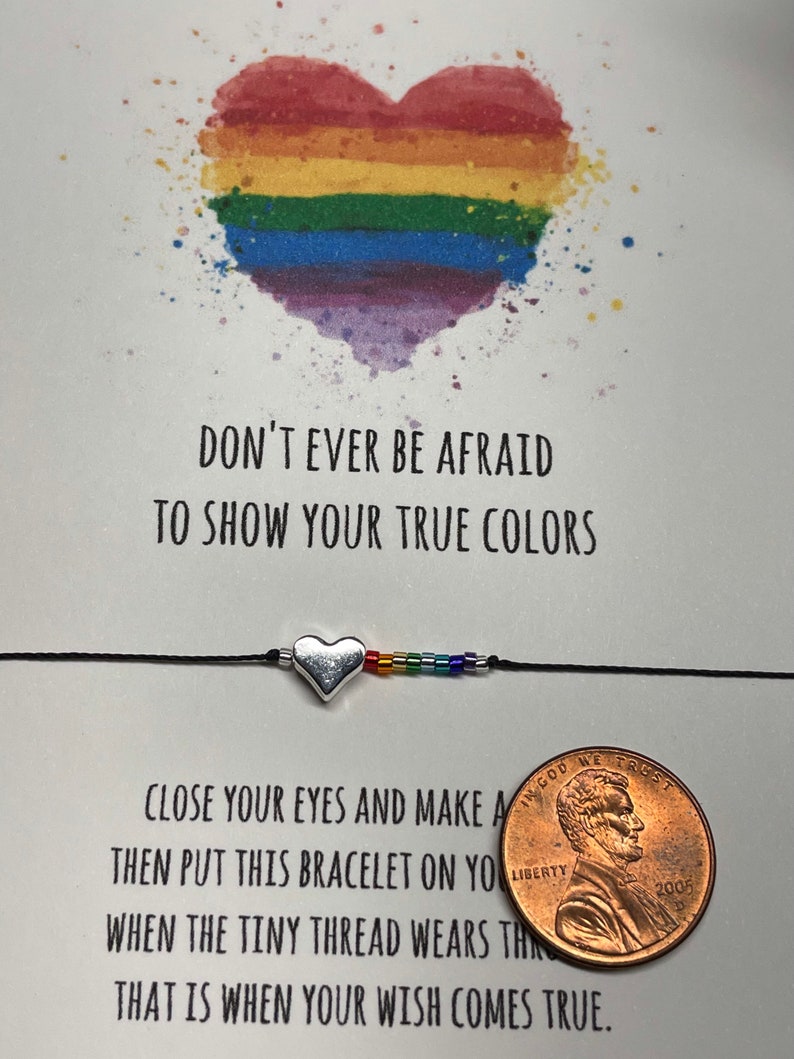 May include: A rainbow heart with the text "Don't ever be afraid to show your true colors."  A black string bracelet with a silver heart charm and rainbow beads. The text "Close your eyes and make a wish, then put this bracelet on your wrist. When the tiny thread wears thin, that is when your wish comes true." is below the bracelet. A penny is in the bottom right corner.