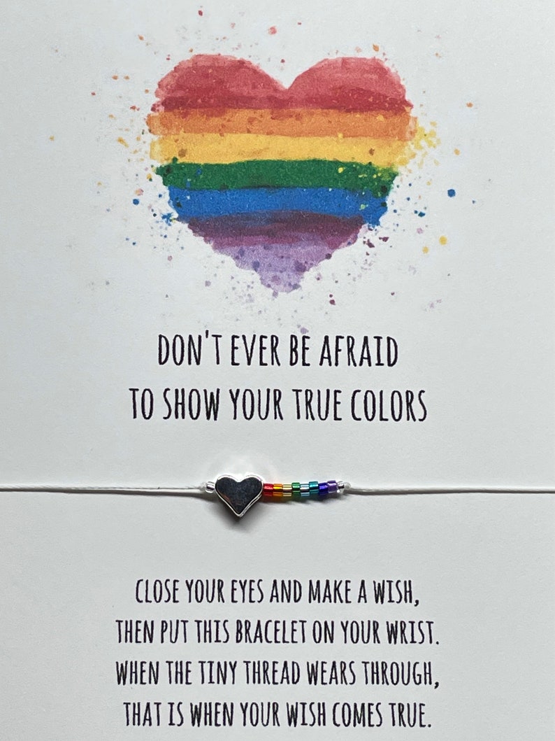 May include: A white card with a rainbow heart and the text "Don't ever be afraid to show your true colors". Below the heart is a silver heart charm bracelet with rainbow beads. The card also includes the text "Close your eyes and make a wish, then put this bracelet on your wrist. When the tiny thread wears through, that is when your wish comes true."