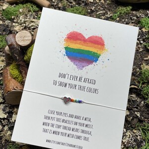 May include: A white card with a rainbow heart and the text "Don't ever be afraid to show your true colors".  The card also includes a rainbow string bracelet with a silver heart charm and the text "Close your eyes and make a wish, then put this bracelet on your wrist. When the tiny thread wears through, that is when your wish comes true. www.etsy.com/shop/2sparrowsstudio"