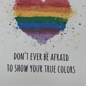 May include: A white card with a rainbow heart and the text "Don't ever be afraid to show your true colors". A rainbow beaded bracelet is at the bottom of the card.