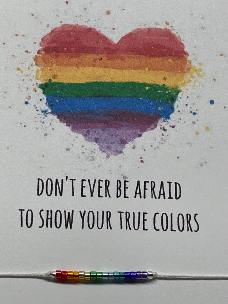 May include: A white card with a rainbow heart and the text "Don't ever be afraid to show your true colors". A rainbow beaded bracelet is at the bottom of the card.