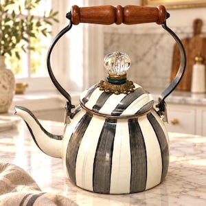 May include: A tea kettle featuring a white and black hand-painted striped pattern on the body and lid. The kettle has a dark metal handle with a wooden grip, a curved spout, and a clear glass knob finial atop a brass-toned decorative base.