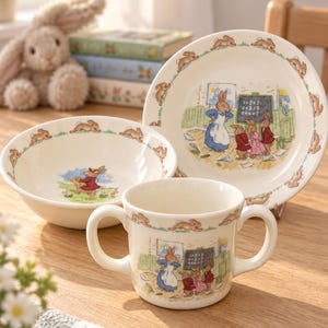 Peut inclure: Un ensemble de vaisselle en céramique comprenant une assiette, un bol et une tasse à deux anses, tous décorés d'illustrations de lapins dans une salle de classe et d'une bordure de lapins en course. Les pièces crème illustrent des lapins.