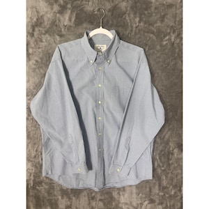 May include: A long-sleeve button-down shirt featuring a small blue and white checkered pattern. The shirt has a pointed collar with buttons at the tips, a front button placket, and buttoned cuffs. A white hanger is inserted through the collar.