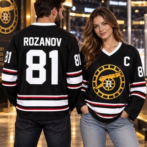 May include: Two black hockey jerseys with white V-necks, featuring white, red, and black stripes on the sleeves and hem. One jersey displays the name ROZANOV and number 81 on the back. The other features a yellow cannon logo and the letter C.
