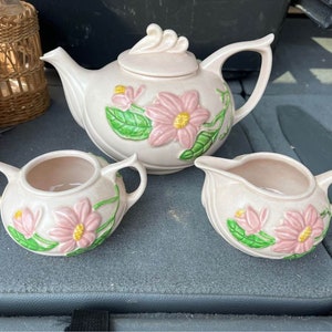 May include: A vintage tea set with a pink floral design. The teapot has a lid and a spout. The creamer and sugar bowl have handles. The set is made of ceramic and has a delicate floral pattern.