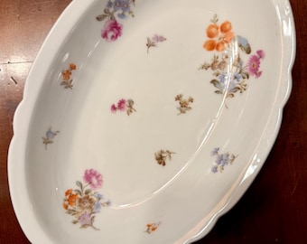 May include: Oval white serving dish with a scalloped edge, decorated with clusters of colorful flowers in pink, orange, blue, and purple. The floral design is scattered across the dish's surface.