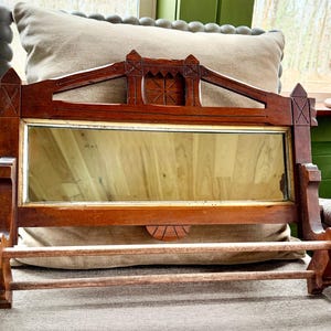 May include: A vintage wooden mirror with a built-in towel rack. The mirror has a rectangular shape with a decorative wooden frame in a rich brown color. The frame features intricate carvings and a small shelf. The towel rack is made of two wooden rods.