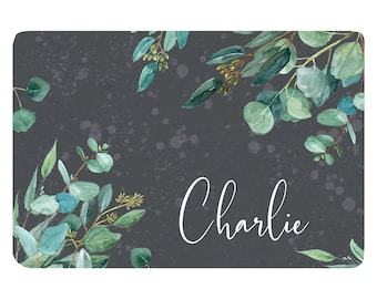Pode incluir: Um fundo cinza escuro com um design de aquarela de folhas e galhos de eucalipto. O nome "Charlie" está escrito em letras cursivas brancas.