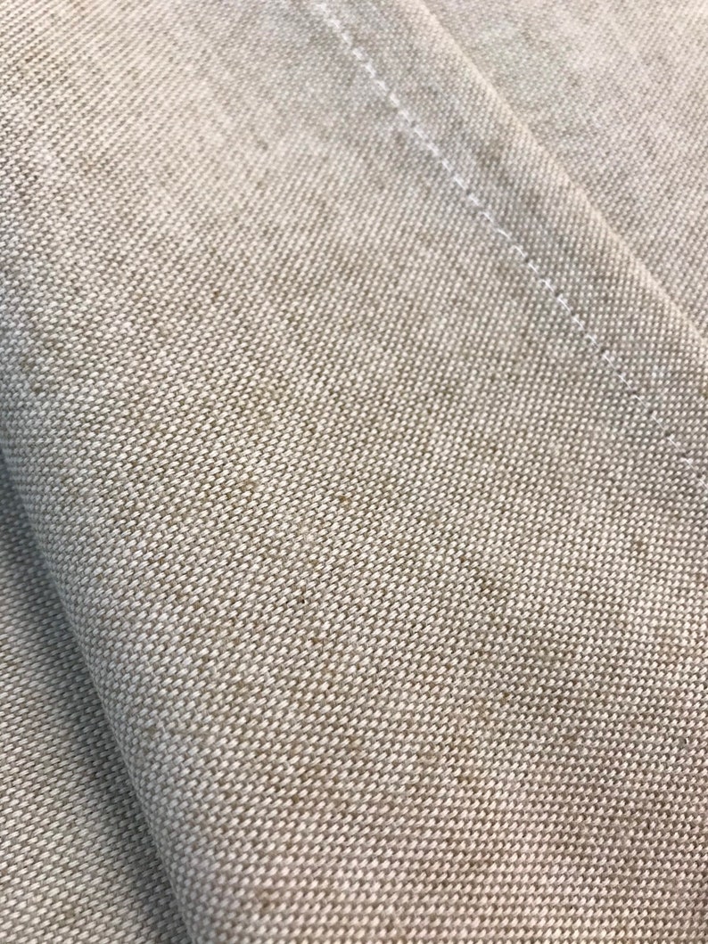 May include: Close-up of a beige fabric with a subtle woven texture. The fabric has a slight sheen and is folded over on itself.