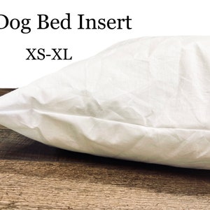 May include: White dog bed insert, labeled "Dog Bed Insert XS-XL". The insert is made of a soft, white fabric and is shown on a wooden surface.