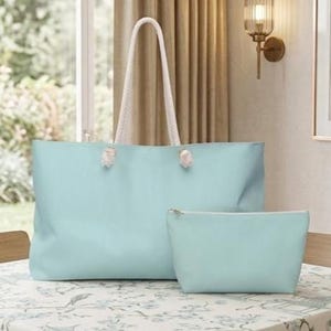 Könnte beinhalten: Eine hellblaue Tragetasche mit weißen Seilgriffen und eine passende hellblaue Reißverschlusstasche. Die Tasche hat eine rechteckige Form und eine glatte Oberfläche, während das kleinere Etui ebenfalls rechteckig mit einem goldenen Reißverschluss ist.
