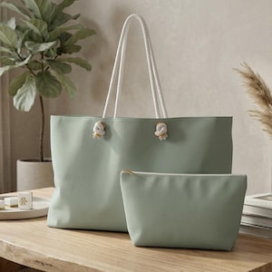 May include: A sage green tote bag with white rope handles and knotted detailing, accompanied by a matching sage green zippered pouch. Both items feature a smooth, solid-coloured exterior and a clean, rectangular design for everyday utility.