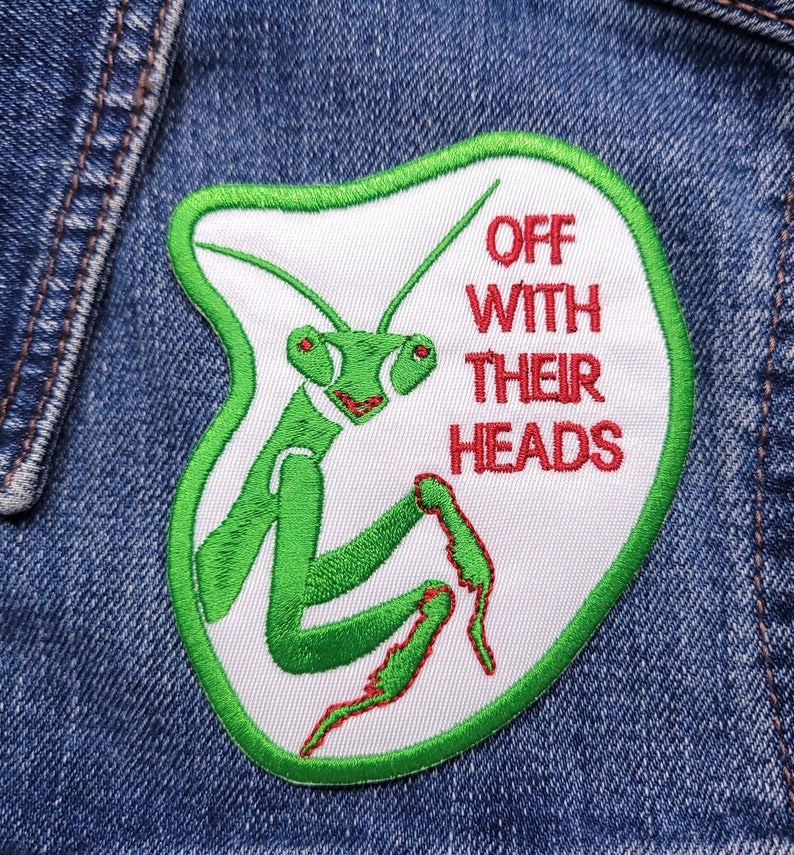 May include: A white patch with green embroidery of a praying mantis and the text "OFF WITH THEIR HEADS" in red.