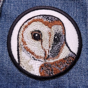 May include: Embroidered patch of a barn owl with brown, white, and black feathers. The owl is in a white circle with a black border.