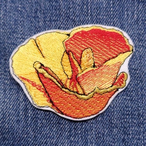 May include: A yellow and red embroidered flower patch. The flower is a stylized poppy with a yellow center and red petals.