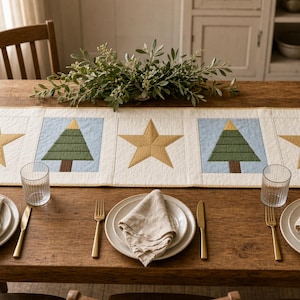 May include: A rectangular quilted table runner featuring a repeating pattern of gold stars and green pine trees on a light blue background, bordered by cream fabric. The runner is displayed on a wooden table with three place settings.