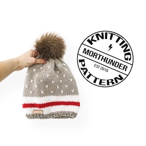 Puede incluir: Un gorro de punto gris y blanco con un pompón de piel sintética marrón. El gorro presenta una franja roja, detalles blancos y una pequeña etiqueta de cuero. La imagen incluye un logotipo circular que dice "Knitting Morthunder Pattern".
