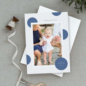 May include: A holiday card with a photo of a family with a baby girl. The card has a blue and white polka dot pattern and the text "Happy Holidays" and "The Taylors" on it.