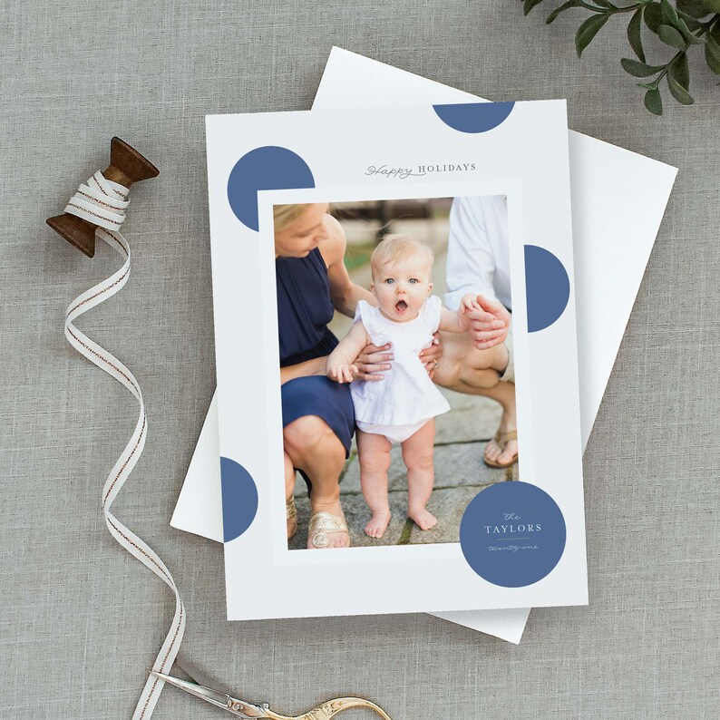 May include: A holiday card with a photo of a family with a baby girl. The card has a blue and white polka dot pattern and the text "Happy Holidays" and "The Taylors" on it.