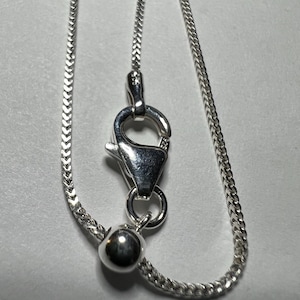 May include: A silver wheat chain necklace featuring a lobster claw clasp and a small round bead at the end. The metal components are stamped with 925, indicating sterling silver. The chain has a woven, textured appearance with a polished finish.