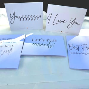 May include: Five rectangular greeting cards. Two white cards feature black cursive text reading YASSSSSS! and I Love You. Three light blue cards feature black text reading To the one who knows me better than I know myself, Let's run errands!, and Best Friend. look how long it's been.