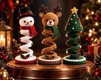 Puede incluir: Tres adornos de ganchillo sobre muelles que representan un muñeco de nieve con sombrero negro y bufanda roja, un reno marrón con bufanda verde y un árbol de Navidad verde con una estrella amarilla, sobre bases circulares con acebo.
