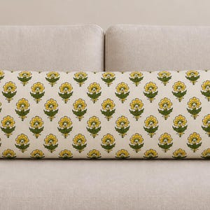 May include: A long rectangular lumbar pillow featuring an off-white background with a repeating pattern of yellow flowers and green leaves. The floral design is arranged in a grid-like formation across the entire surface of the fabric cover.