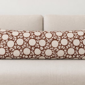 May include: A rectangular lumbar pillow featuring a repeating pattern of dark brown circular floral motifs and interconnected leafy vines set against a solid off-white background. The pillow has a structured, elongated shape with clean edges.