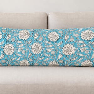 Könnte beinhalten: Ein langes, rechteckiges Lendenkissen mit einem leuchtend türkisblauen Hintergrund und einem sich wiederholenden Muster aus cremeweißen Blumen, Blättern und Stängeln. Das florale Design bedeckt die gesamte Oberfläche des Kissens und zeigt detaillierte Blütenblätter.