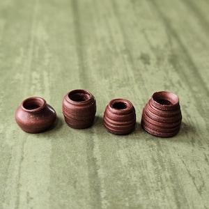 May include: Four small, brown, decorative pottery vases of varying shapes and sizes are arranged in a row. The vases have a rustic, handmade appearance, with visible texture and a warm, earthy color.