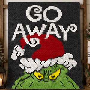 May include: A rectangular quilt featuring a black background with the white pixelated text GO AWAY. Below the text is a red Santa hat with white trim, positioned above a green character with yellow eyes, all rendered in a pixelated block style.