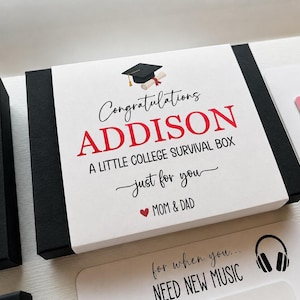 Op de afbeelding: Een zwart-witte geschenkdoos met een papieren wikkel voorzien van een icoon van een afstudeerhoed en de tekst Congratulations ADDISON A LITTLE COLLEGE SURVIVAL BOX just for you MOM & DAD. Extra kaarten met tekst en een koptelefoonicoon zijn zichtbaar.