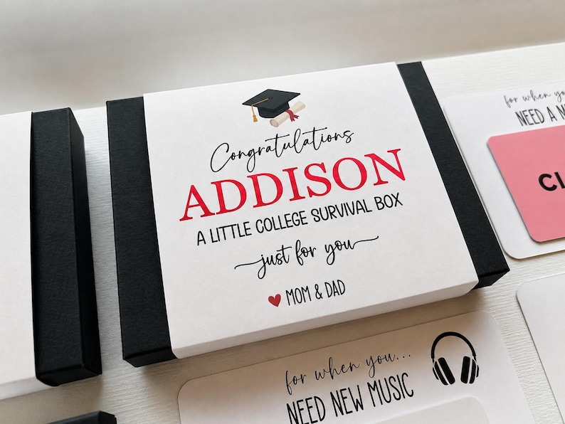 Op de afbeelding: Een zwart-witte geschenkdoos met een papieren wikkel voorzien van een icoon van een afstudeerhoed en de tekst Congratulations ADDISON A LITTLE COLLEGE SURVIVAL BOX just for you MOM & DAD. Extra kaarten met tekst en een koptelefoonicoon zijn zichtbaar.